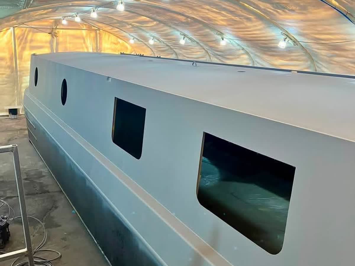 The wide-beam hull under cover, window apertures cut, August 2026